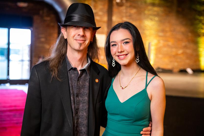 A man wearing black smiles with a woman in a teal dress